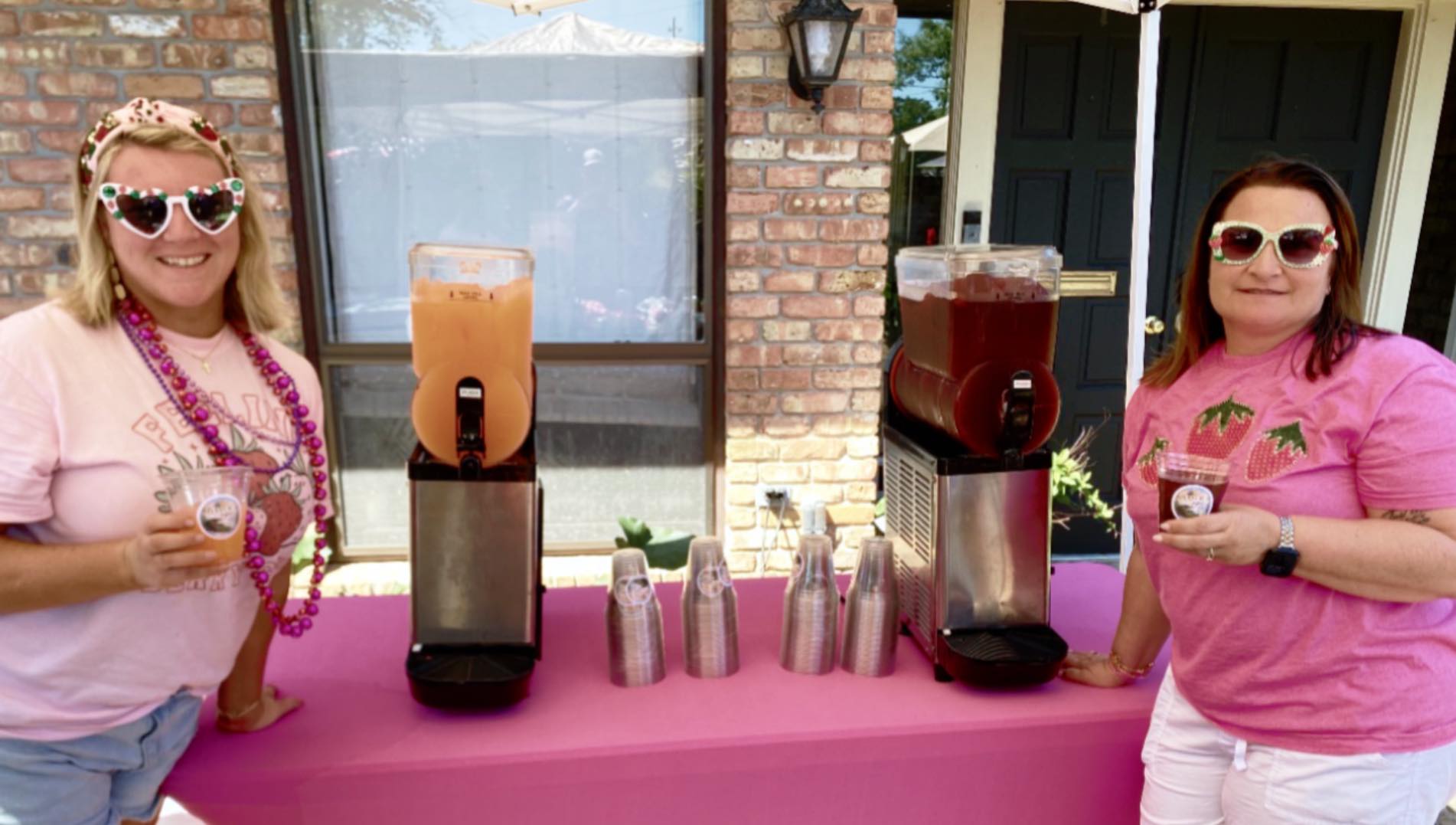 The owners of Bayou Sips standing behind two frozen drink machines at an event